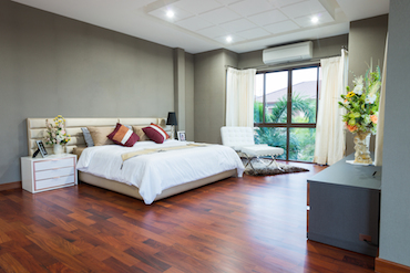 a carpeted room witha high sloping ceiling, two small bright windows, and a a two-person bed with a bedside table and lamp on each side